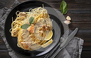 Spaghetti , pasta  with chicken fillet, lemon slices,  greens, spinach, garlic, on a black plate on  dark,  napkin, fork, knife