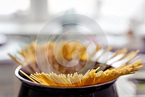 Spaghetti pasta cooking in a black pot on a gas stove, old apartment kitchen, fire and steam