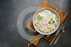 Spaghetti pasta with creamy mushroom sauce on a on wooden cutting board, gray rustic background. Italian traditional dish. Top