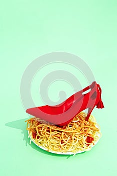 Spaghetti pasta with ketchup and red lady shoes on green background. Minimalism.  Diet, calory Italian food art concept