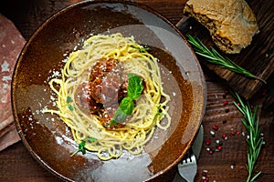 Spaghetti pasta and meat balls in tomato sauce in brown plate with Basil and Parmesan on wooden background