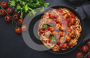 Spaghetti pasta with meatballs in tomato sauce with parsley in frying pan, dark table background, top view