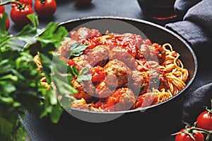 Spaghetti pasta with meatballs in tomato sauce with parsley in frying pan with sangiovese red wine, dark table background, top