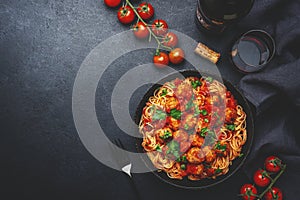 Spaghetti pasta with meatballs in tomato sauce with parsley in frying pan with sangiovese red wine, dark table background, top