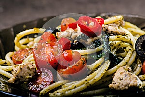 Spaghetti pasta with olive oil, tomatoes, herbs, chilly, and cut chicken breast. Italian cuisine. Plate with food on a black table