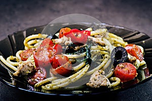 Spaghetti pasta with olive oil, tomatoes, herbs, chilly, and cut chicken breast. Italian cuisine. Plate with food on a black table