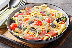 Spaghetti pasta with olives, tomatoes, onions, cucumbers and bell pepper close-up in a bowl. horizontal