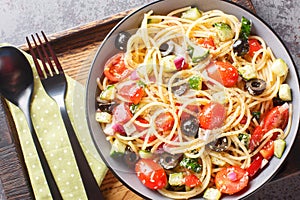Spaghetti pasta with olives, tomatoes, onions, cucumbers and bell pepper close-up in a bowl. horizontal top view
