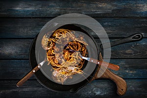 Spaghetti. Pasta with seafood on a hot frying pan with a spoon and fork on a colored wooden background. Top view