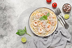 Spaghetti pasta with shrimp in a creamy sauce in a plate on a light stone background. Top view, flat lay, copy space.