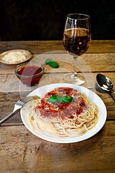 Spaghetti Pasta with Tomato Sauce, Chees and Basil with White Wine Glass on Wooden Table. Traditional Italian Food