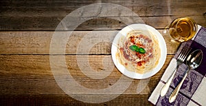 Spaghetti Pasta with Tomato Sauce, Cheese, Basil and White Wine Glass on Wooden Table. Traditional Italian Food.