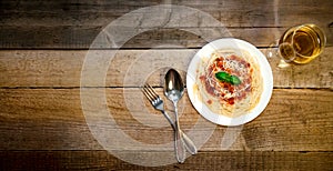 Spaghetti Pasta with Tomato Sauce, Cheese, Basil and White Wine Glass on Wooden Table. Traditional Italian Food.