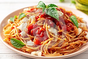 Spaghetti pasta with tomato sauce, mozzarella cheese and fresh basil in plate on white wooden background