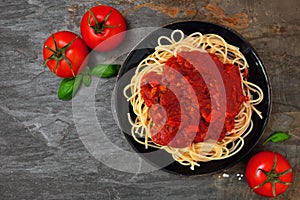 Spaghetti pasta with tomato sauce, peppers and mushrooms, above view on a dark stone background