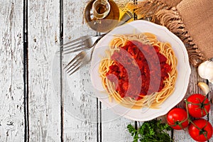 Spaghetti pasta with tomato sauce, peppers and mushrooms, top view corner border on a white wood background with copy space