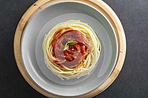 Spaghetti pasta with tomatoes sauce and basil in plate on dark background. Pasta plate isolated. Top view with copy space