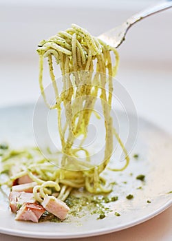 Spaghetti with pesto and ham slices are on the plate