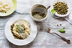 Spaghetti with pesto sauce on white vintage plate, grated cheese, fresh basil leaves and green beans on wooden background