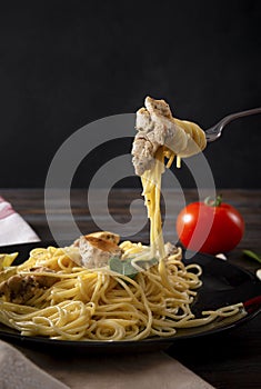 Spaghetti with a piece of chicken fillet on a fork on a dark background,  plate of pasta, tomato, napkin
