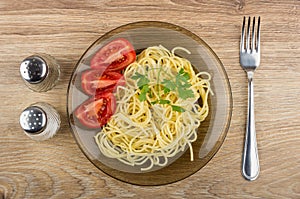 Spaghetti in plate with tomatoes, parsley, salt, pepper and fork