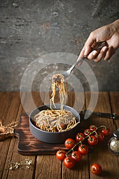 Spaghetti is pulled up by the fork in hand from dish and wooden plate