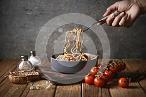 Spaghetti is pulled up by the fork in hand from dish and wooden plate