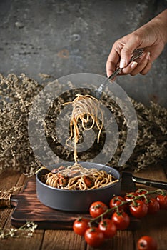 Spaghetti is pulled up by the fork in hand from dish and wooden plate for serving with homemade environment on classic