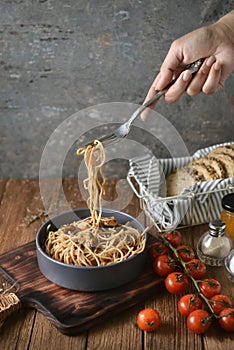 Spaghetti is pulled up by the fork in hand from dish and wooden plate for serving with homemade environment on classic