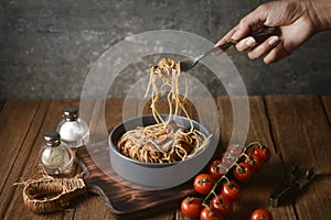 Spaghetti is pulled up by the fork in hand from dish and wooden plate for serving with homemade environment on classic