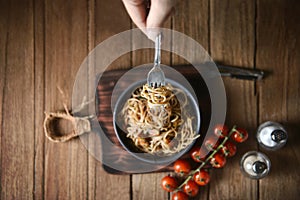 Spaghetti is pulled up by the fork in hand from dish and wooden plate for serving with homemade environment on classic