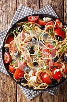 Spaghetti salad with feta, olives, tomatoes and parsley close-up on a plate.Vertical top view