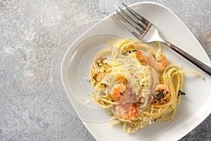 Spaghetti with shrimps, parsley and garlic, Mediterranean seafood appetizer on a plate, rustic gray background with copy space,