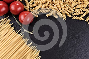 Spaghetti, spirelli and cherry tomatoes on black slate plate