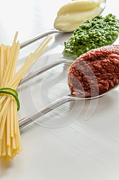 Spaghetti and three spoons with different condiments