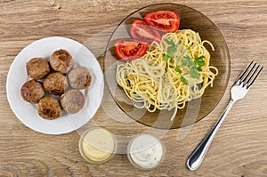 Spaghetti with tomatoes, parsley, plate with meatballs, bowls wi