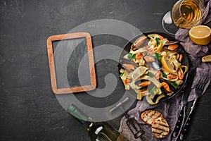 Spaghetti vongole, Italian seafood pasta with clams and mussels, in plate with herbs and glass of white wine on rustic stone