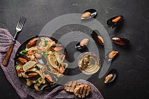 Spaghetti vongole, Italian seafood pasta with clams and mussels, in plate with herbs and glass of white wine on rustic stone