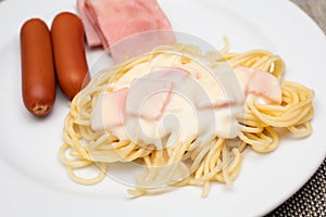 Spaghetti white sauce with ham and sausage serving on white plate. Traditional western food.