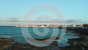 Spain, Canary Islands, Fuerteventura. Volcanic beach in low tide. Blue ocean landscape. Cityscape of resort town