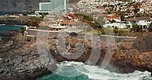 SPAIN CANARY ISLANDs TENERIFE 2023 April: Red medical helicopter, rescuer lowered to the rocky shore over stormy ocean