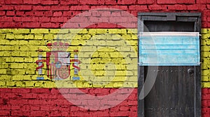 Spain flag painted on brick wall and closed door with medical mask protected