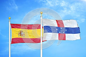 Spain and Netherlands Antilles two flags on flagpoles and blue cloudy sky