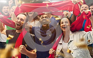 Spainian football, soccer fans cheering their team with a red scarfs at stadium. Excited fans cheering a goal