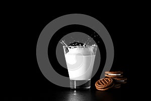 Spalsh in glass of milk and chocolate cookies on black background