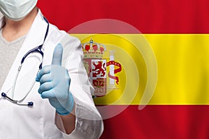 Spanish doctor`s hand showing thumb up positive gesture on flag of Spain background