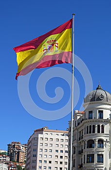 Spanish flag flying over the city, under a clear blue sky