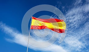 Spanish flag on a pole, undulating in the wind on blue sky with soft white clouds