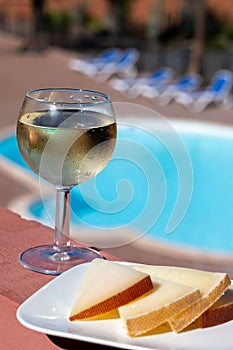 Spanish hard manchego, cow, sheep and goat cheese, cold white wine and blue swimming pool on background