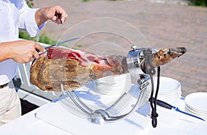 Spanish Iberian ham or Pata Negra mounted on a wooden stand with a butcher cutting slices of it